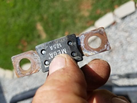 1988 Ford Bronco - A hand holds a MEGA 175A fuse with corroded terminal ends. The fuse is black with silver lettering and has two circular holes for mounting.
