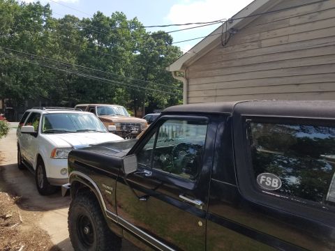 1988 Ford Bronco - A black 1988 Ford Bronco is parked next to a white SUV and a brown pickup truck in a driveway next to a house.