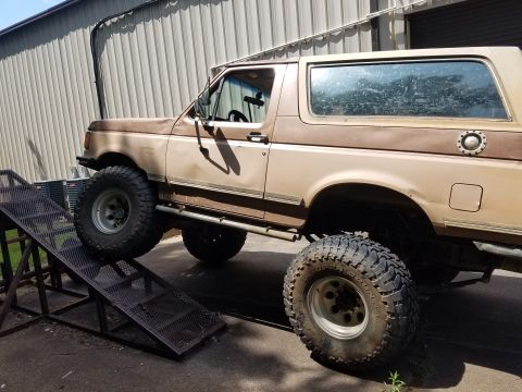 1988 Ford Bronco - A lifted two-tone brown 1988 Ford Bronco is positioned on a metal ramp, with its front tire on the ramp and its rear tire on the ground.