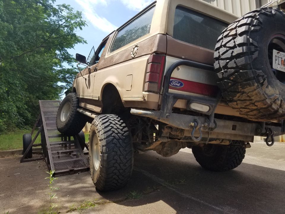 Lifted 1980s Ford Bronco on a ramp, rear driver's side view.