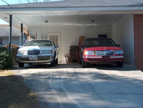 2001 Ford Crown Victoria - Two sedans are parked under a carport, one white and one red.