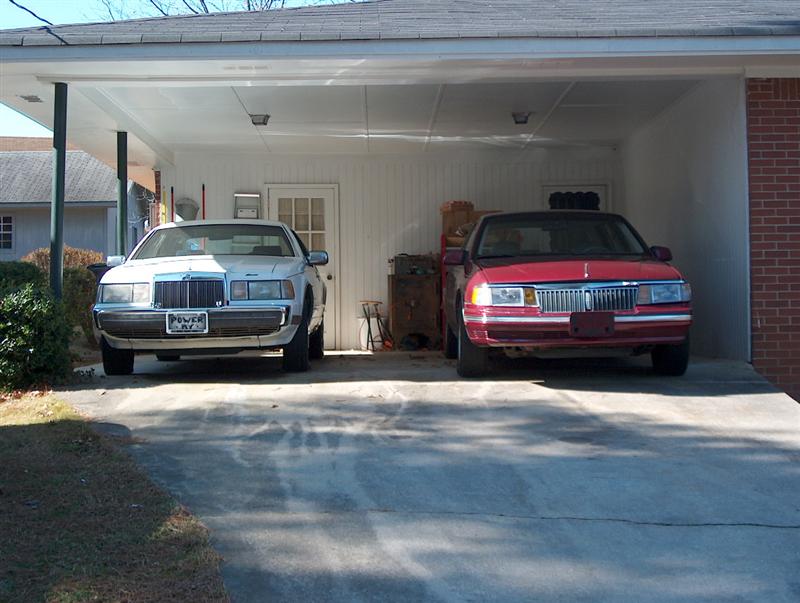 White sedan and red sedan parked side-by-side in a carport