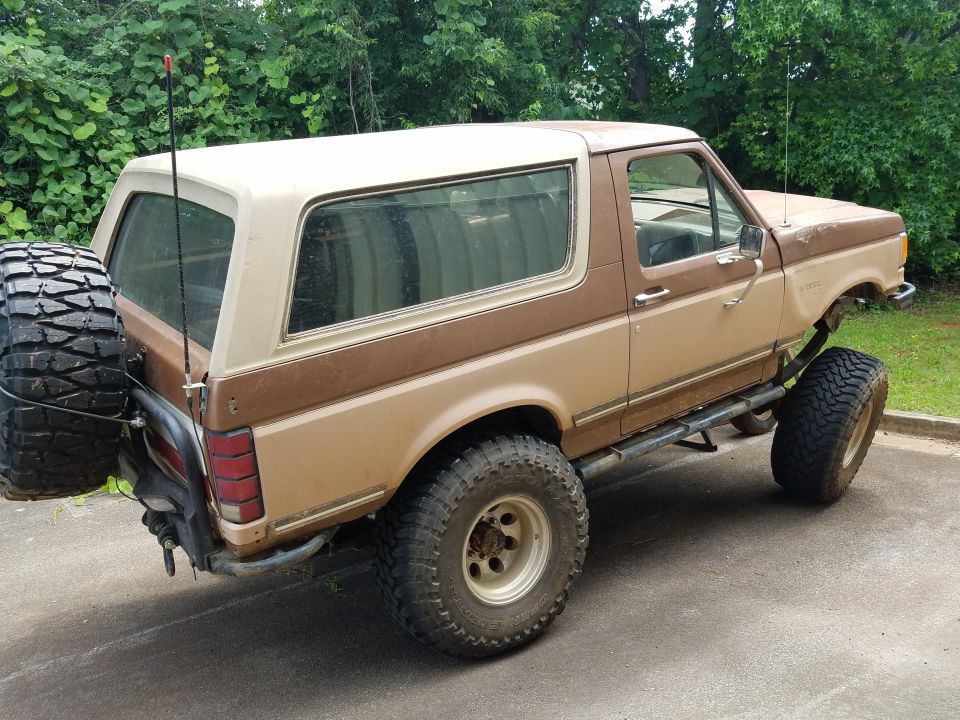 Lifted 1980s Ford Bronco with spare tire on rear, parked outdoors.