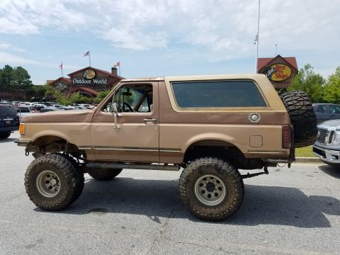 1988 Ford Bronco - A lifted, two-tone brown 1988 Ford Bronco is parked in a parking lot in front of Bass Pro Shops and Outdoor World. The vehicle has large of…