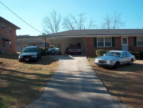2001 Ford Crown Victoria - A collection of vehicles are parked in the driveway and yard of a residential property on a sunny day.