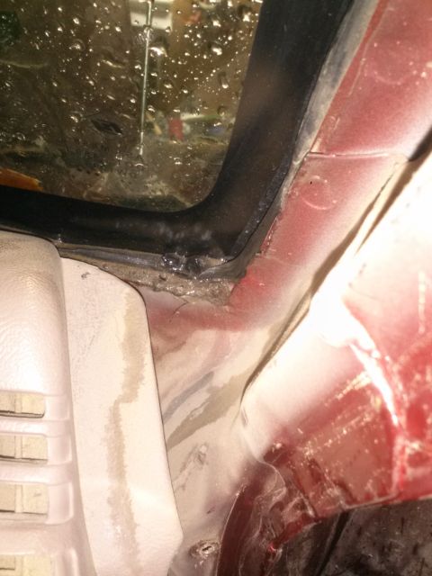 1996 Ford Bronco - A close-up view of the interior of a red vehicle, showing the seal around a window and the surrounding bodywork. Water droplets are visible…