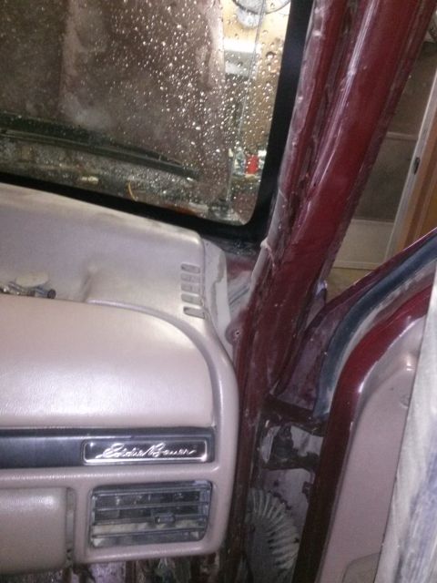 1996 Ford Bronco - Interior view of a maroon vehicle, showing the dashboard with an Eddie Bauer emblem and an air vent. The windshield is covered in water dro…
