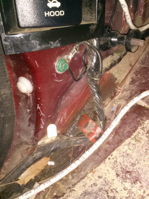 1996 Ford Bronco - A close-up view of wiring and a ground strap attached to the red painted interior of a vehicle, with a "HOOD" release button visible in the…
