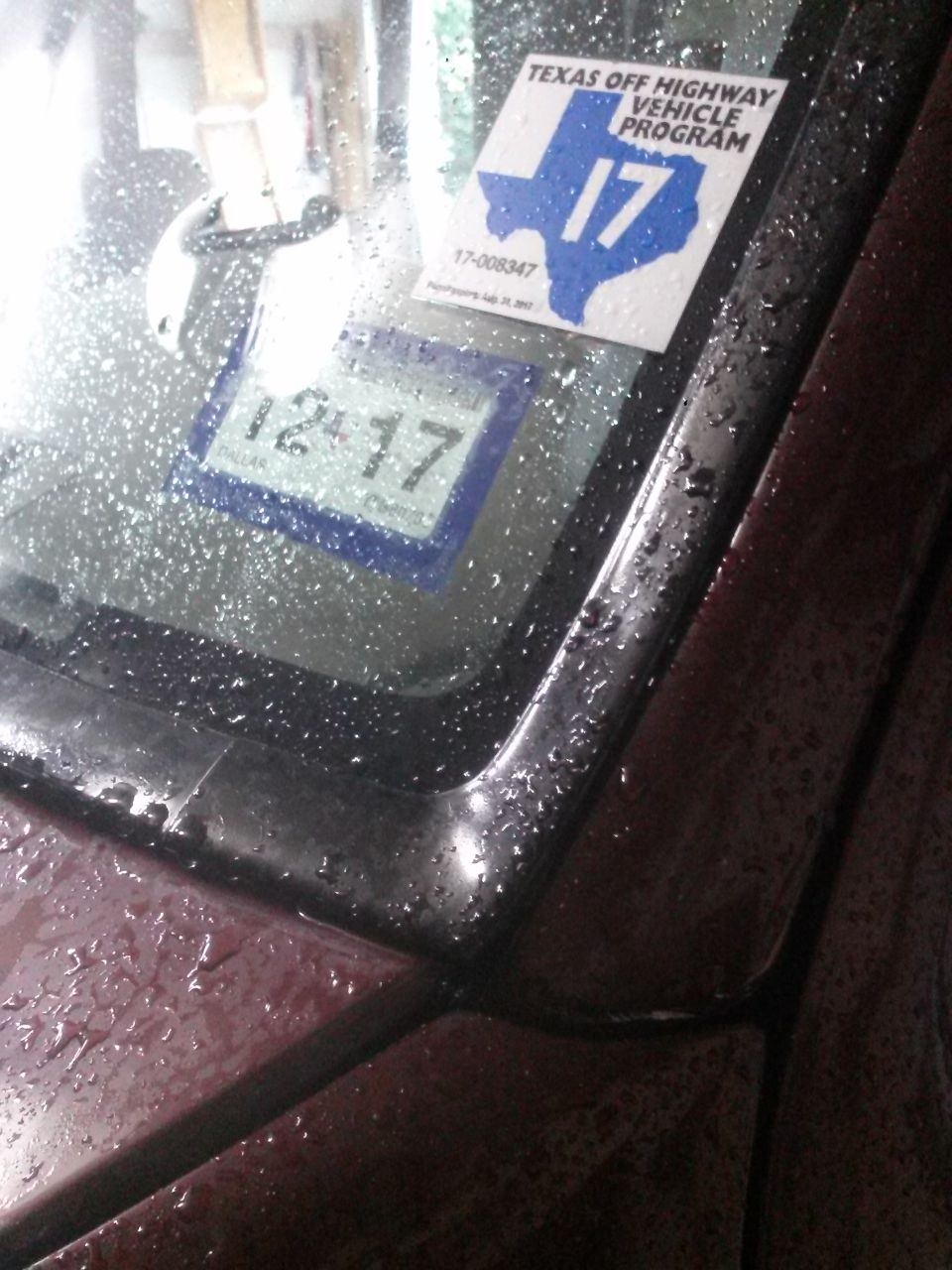 Close-up of vehicle windshield with rain, Texas OHV sticker, and 12/17 registration sticker.