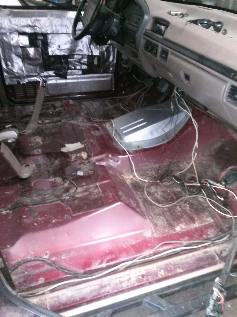 Interior of a 1996 Ford Bronco with floor stripped for modifications, showing sound deadening on the door and wires.