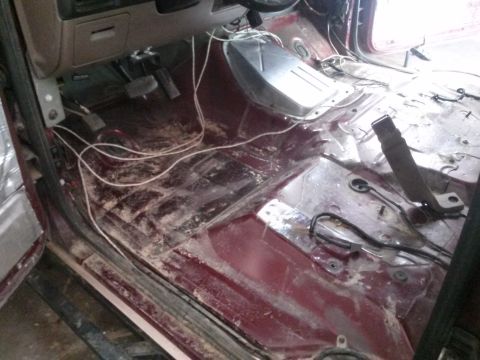 1996 Ford Bronco - The interior of a vehicle is shown with the floor removed, revealing the chassis and wiring. The dashboard, pedals, and part of the center…