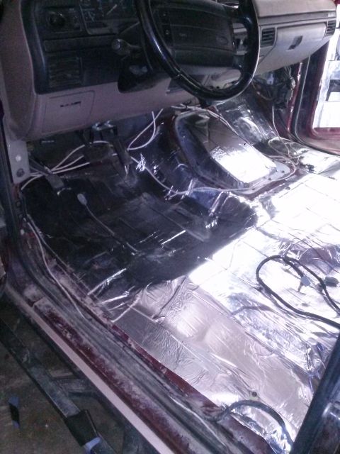 1996 Ford Bronco - The interior of a vehicle is shown with the floor covered in sound deadening material. The dashboard and steering wheel are visible, along…