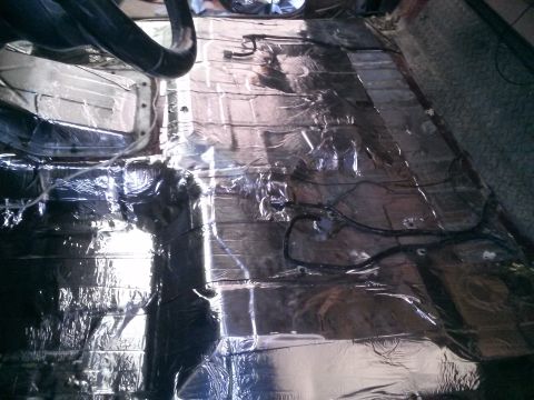 1996 Ford Bronco - The interior floor of a vehicle is covered in sound deadening material and wiring. A black tube or pipe is visible in the upper left corner.