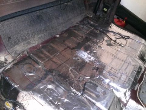 1996 Ford Bronco - The interior floor of a vehicle is covered in silver sound-deadening material and wiring. A red gas can is visible in the background.