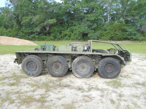 1992 Ford Bronco - A large, olive-drab, six-wheeled military vehicle sits parked on a sandy, grassy area with trees in the background. The vehicle appears to…