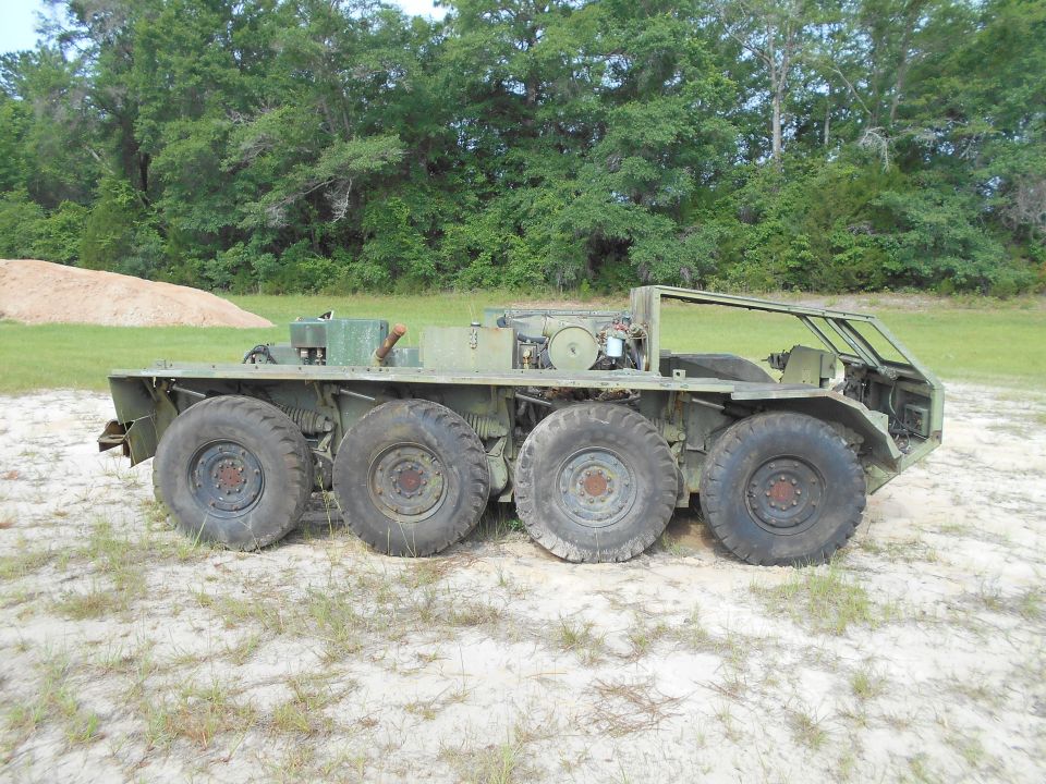 Olive-drab military vehicle with six large wheels and an open cab.