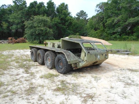 1992 Ford Bronco - A heavily weathered, olive drab, six-wheeled amphibious military vehicle sits in a sandy, grassy area with trees in the background. The veh…