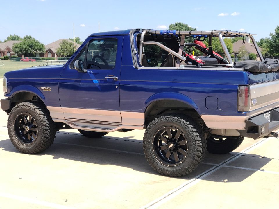 Lifted blue 1996 Ford Bronco with tan stripe and roll cage, side view.