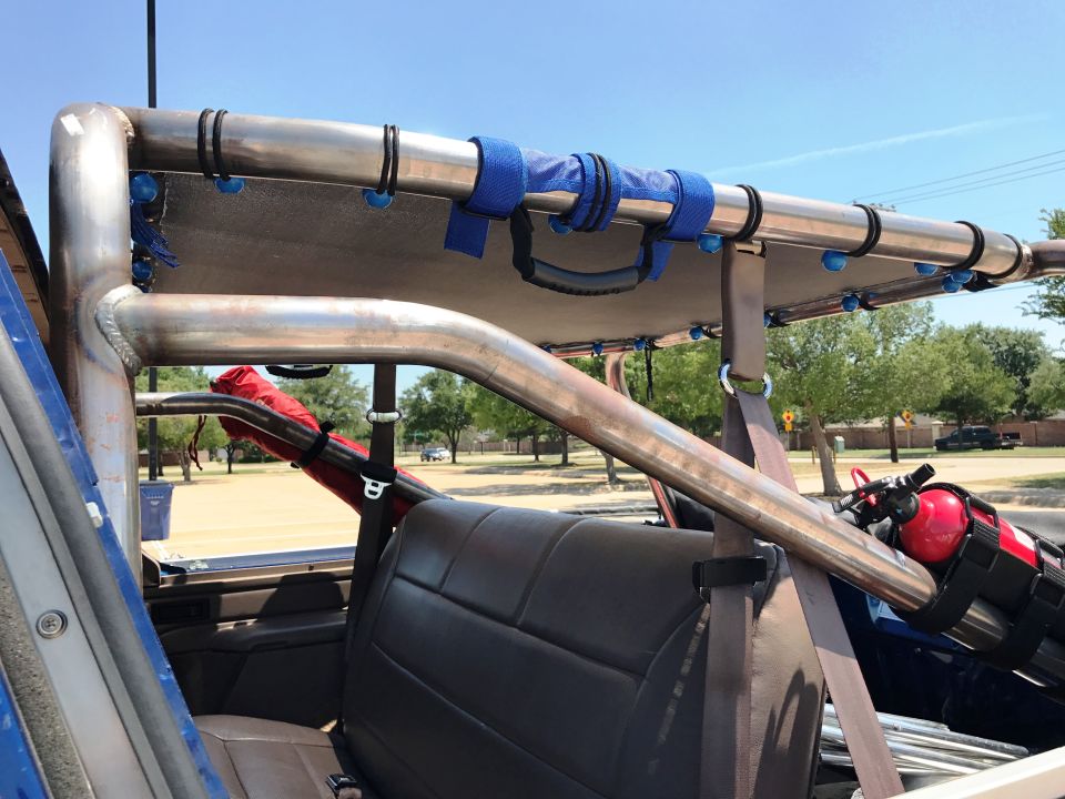 Interior of a modified vehicle with roll cage, sunshade, and fire extinguisher.