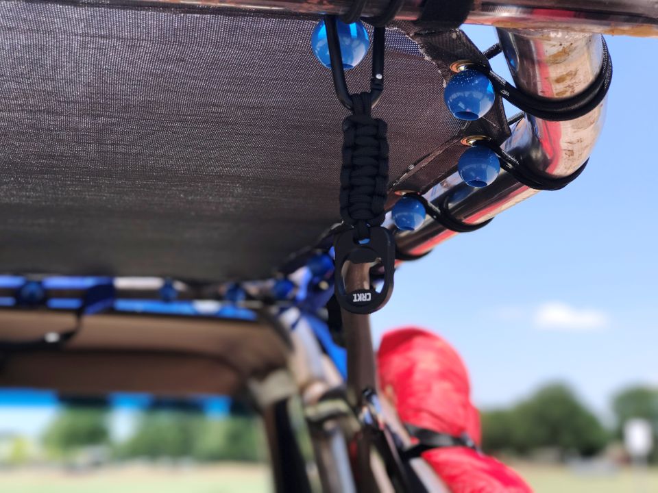 CRKT bottle opener on a paracord lanyard hanging from a roll cage with blue beads.
