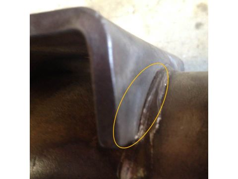 1979 Ford Bronco - A close-up, angled view of a metal part, possibly a bracket or mounting piece, showing signs of wear and damage. The part is dark brown and…