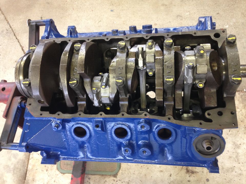 Blue Ford V8 engine block with crankshaft and connecting rods installed on a red engine stand.