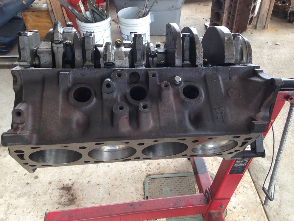 Cast iron engine block with crankshaft and connecting rods on a red engine stand.