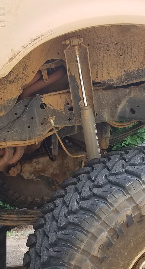 1988 Ford Bronco - A close-up view of the rear suspension of a lifted 1988 Ford Bronco, showing a shock absorber, leaf springs, and a portion of a large off-r…