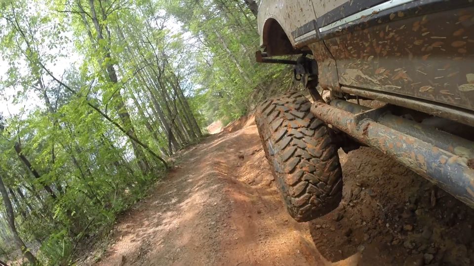 Muddy tire and side of a tan off-road vehicle on a forest trail.
