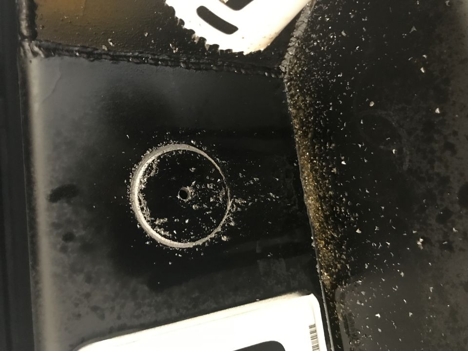 Metal shavings around a drilled hole in black painted metal, with a hole saw blade visible.
