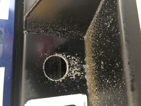 1996 Ford Bronco - A close-up view of a black metal component with a freshly drilled hole and metal shavings scattered around it. The surface appears to be pa…
