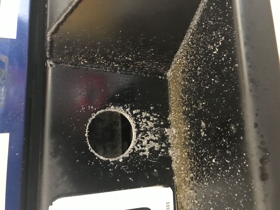 Close-up of black metal with a drilled hole and metal shavings.