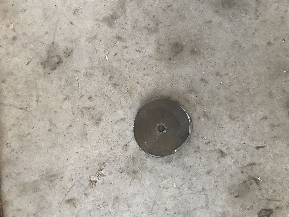 A metal disc with a hole in the center on a concrete surface.