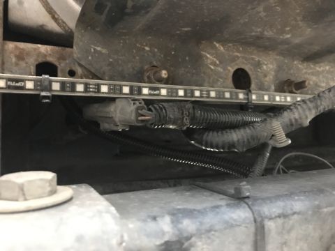 1996 Ford Bronco - A close-up view shows a strip of LED lights mounted with zip ties beneath a vehicle's frame, with wiring and a grey electrical connector vi…
