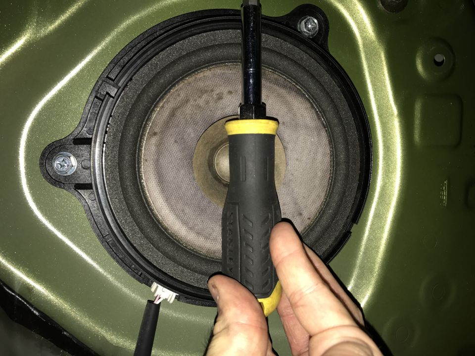 Screwdriver removing speaker from green car door panel