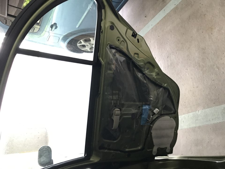 Interior of a car door with the inner panel removed, showing wiring and a plastic moisture barrier.