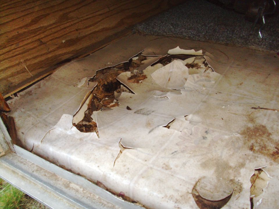 Damaged trailer floor with torn linoleum and rot
