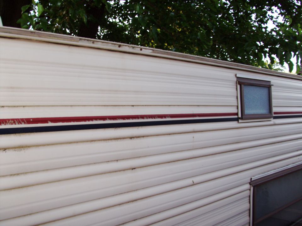 Side view of a beige mobile home with a red and black stripe and a small window.