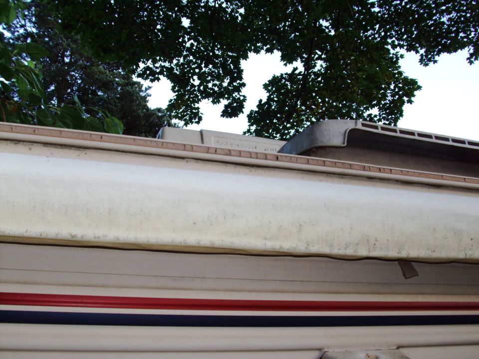 Close-up of an extended RV awning with red and blue stripes on the vehicle body.