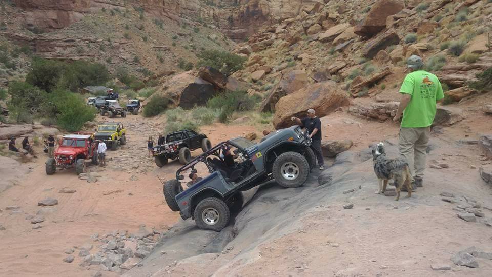 Off-road vehicles on a rocky desert trail with a Jeep climbing a steep incline.