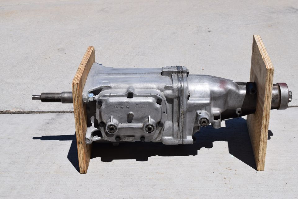 Silver manual transmission with splined input shaft and yoke, mounted on wooden blocks.