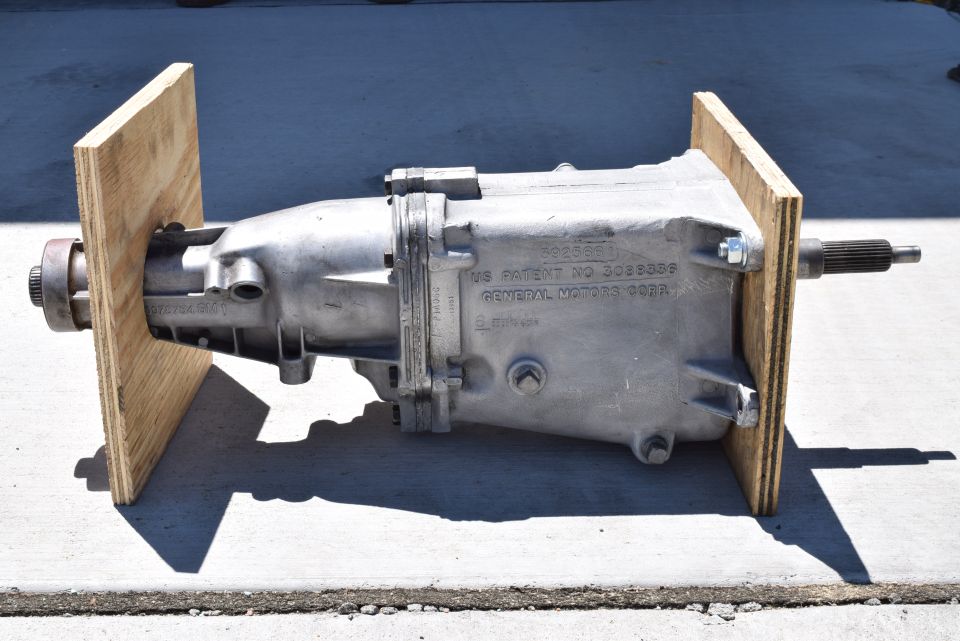 Silver transmission case with patent information, supported by plywood.