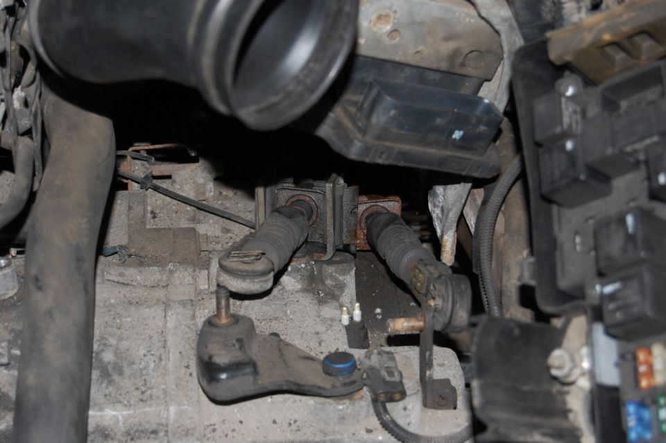 Close-up of dirty manual transmission shift linkage with rubber boots and metal parts.