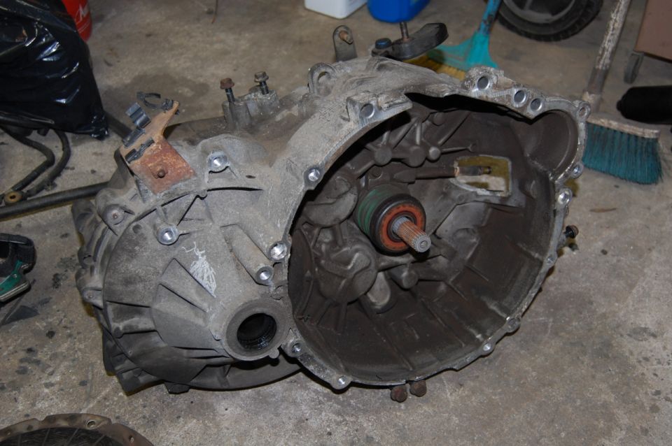 Dusty manual transmission with visible internal components and pilot bearing on concrete floor