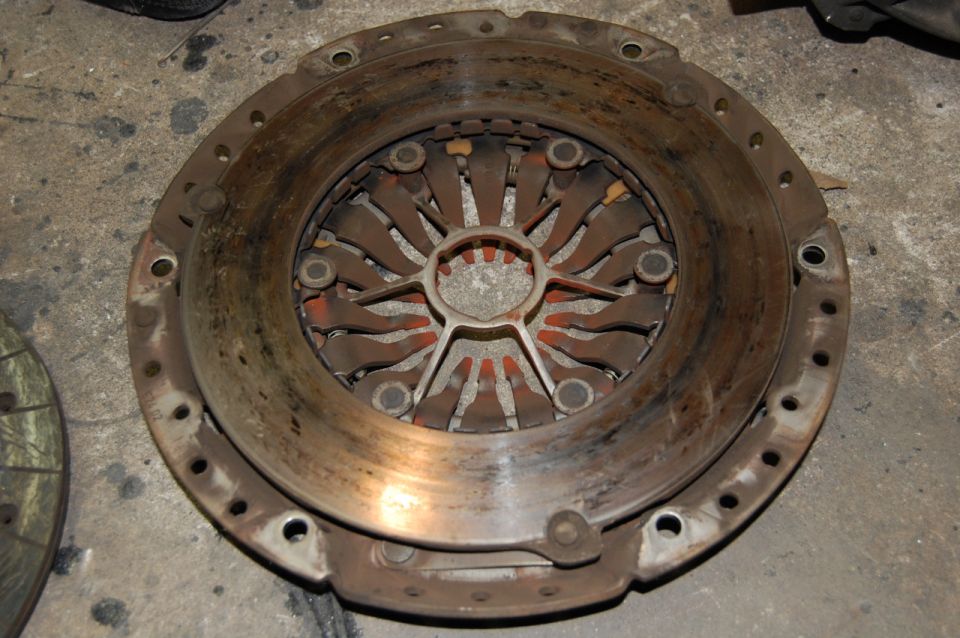 Close-up of a used clutch pressure plate assembly on a concrete floor.