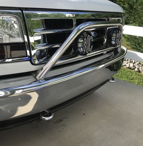 1995 Ford Bronco - The front grille and chrome bumper of a white Ford Bronco are visible, featuring a chrome bull bar with two KC lights mounted on it. Two to…
