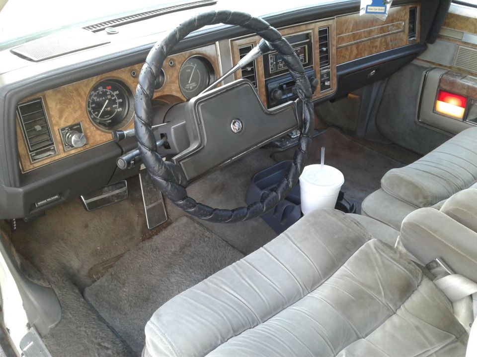 car interior with wood trim, analog gauges, and cloth seats. Cup in holder
