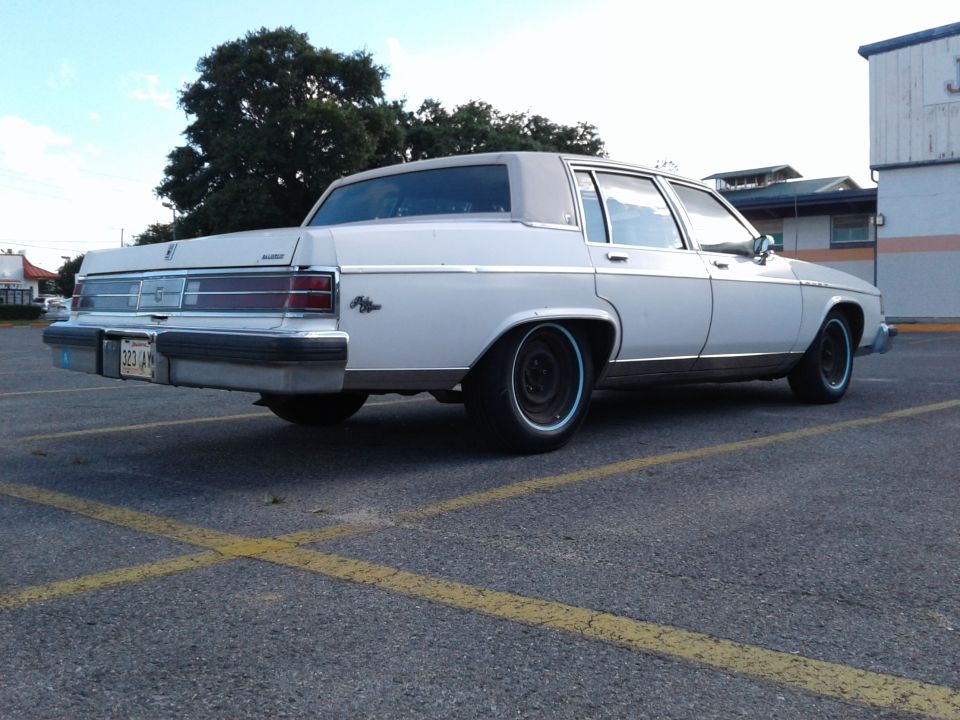 White sedan parked in a lot, rear view. Blue trim on wheels