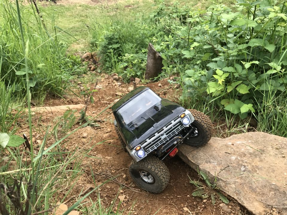 Black RC rock crawler truck with large tires driving over a rock on a dirt path