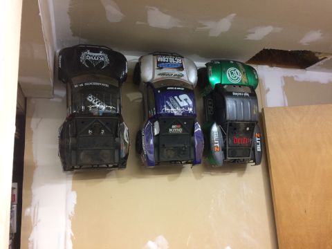1989 Ford Bronco - Three remote control car bodies are mounted on a wall, each with distinct racing decals and sponsor logos.